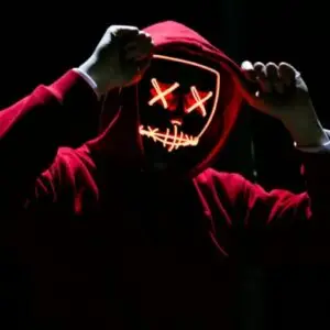 A spooky illuminated mask figure with a red hoodie in a dark setting, perfect for Halloween themes.